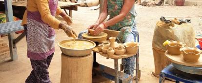 A Cambodian woman teaches a senior volunteer traditional Khmer pottery. An older volunteer participates in a pottery class as part of her Khmer cultural experience in Cambodia.